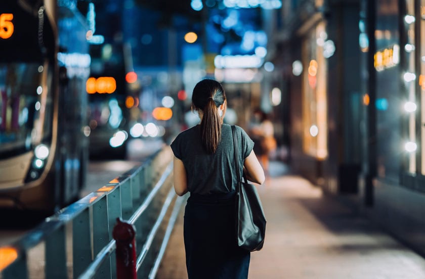 Woman walking on busy downtown city street after work at night
